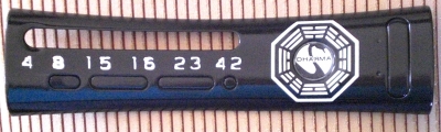 Simple glossy black plate with the Dharma logo for the Swan Outpost, and Hurley's mysterious numbers.